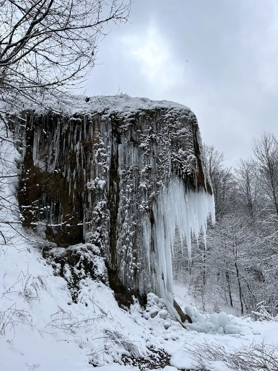 Prskalo waterfall frozen in winter — the rock under icicles, snow in the forest around it